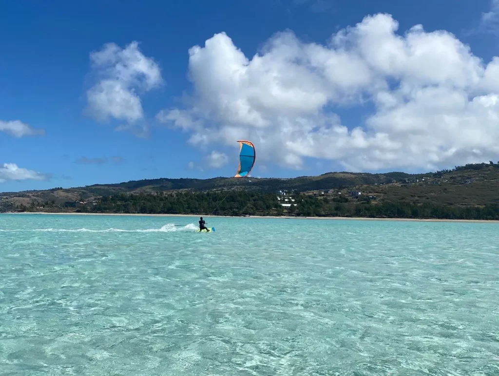 Un kitesurfeur navigue au loin sur un immense lagon d'eau turquoise et cristalline face aux collines verdoyantes de l'île Rodrigues.