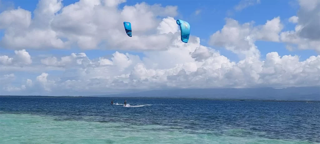 Deux kitesurfeurs naviguent sur une mer aux nuances turquoise et bleue sous un ciel nuageux aux Antilles françaises.