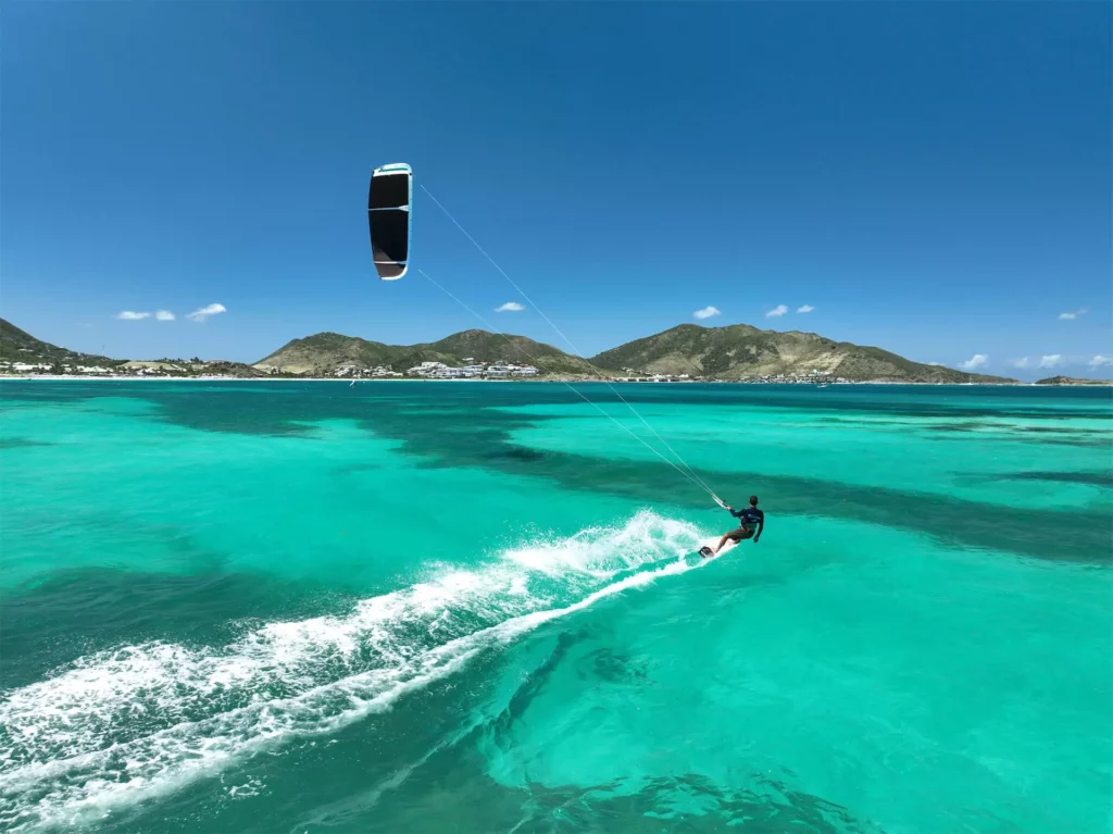 Un kitesurfeur glisse de manière dynamique sur une eau lagon turquoise translucide face aux collines de Saint-Martin.