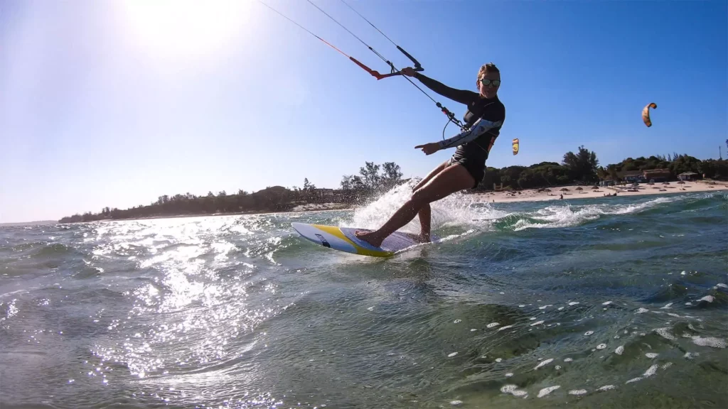 Une kitesurfeuse équipée de lunettes de soleil glisse sur l'eau en tirant un bord face au soleil à Bilene au Mozambique.