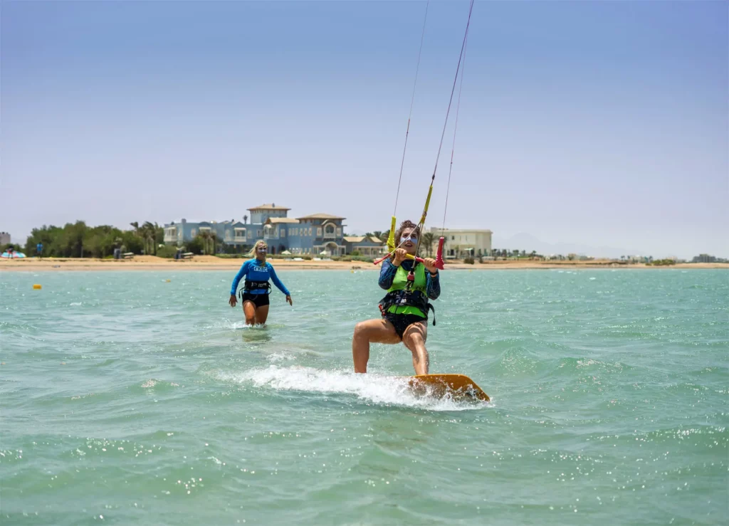 Une kitesurfeuse glisse sur l'eau turquoise d'une lagune peu profonde tandis qu'une autre femme marche derrière elle à El Gouna en Égypte.