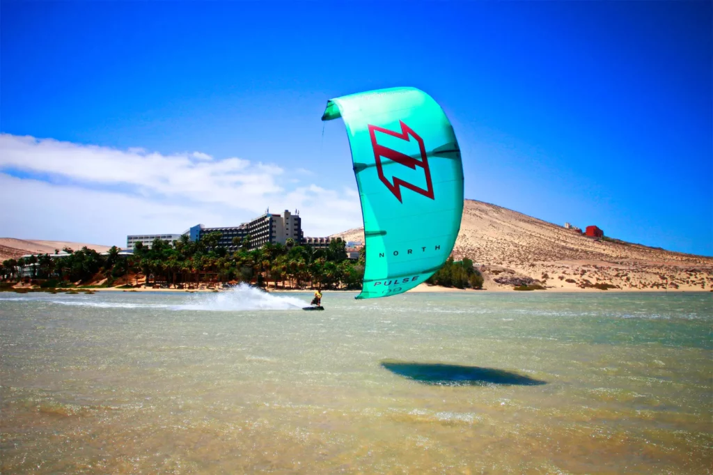 Un kitesurfeur navigue avec une aile turquoise North Pulse sur une lagune peu profonde à Fuerteventura.