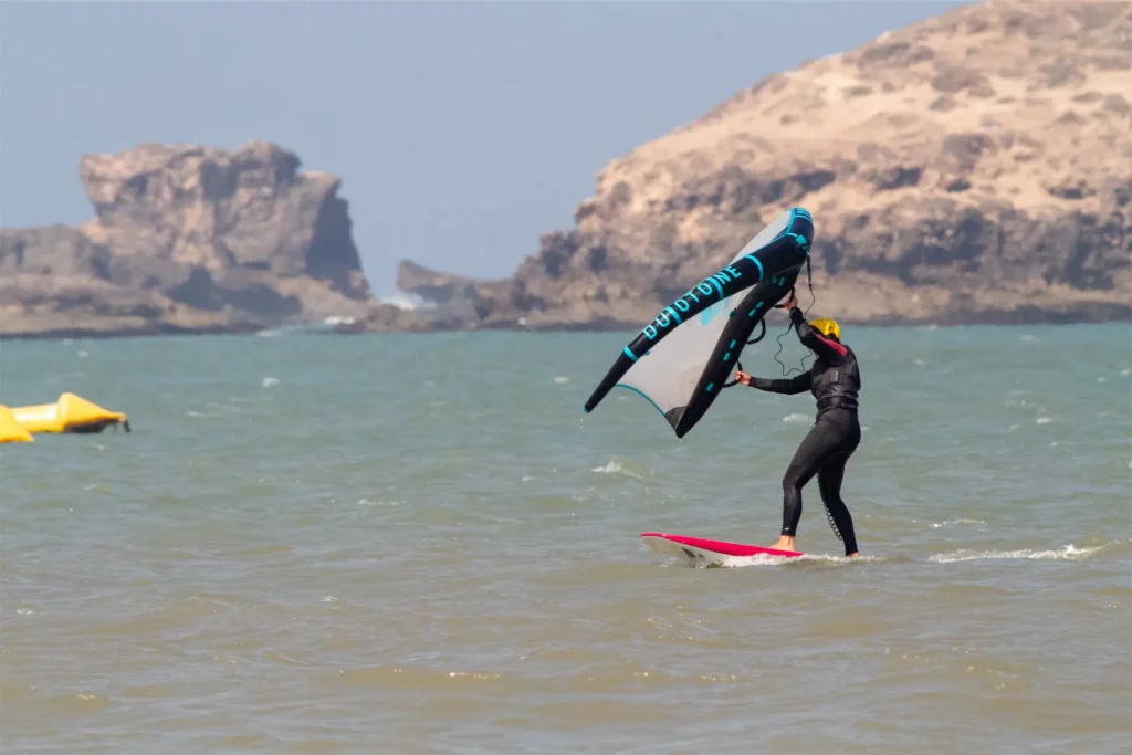 Pratique du wingfoil à Essaouira au Maroc avec les falises de l'île de Mogador en arrière-plan.