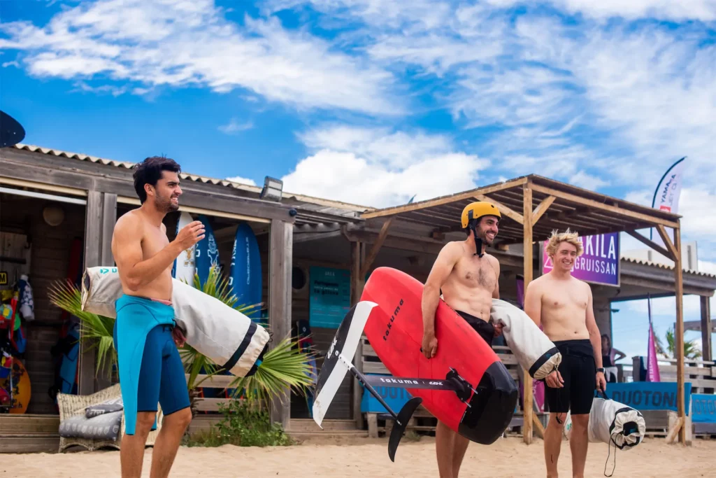 Trois hommes sortant d'un club de glisse Akila à Gruissan en France avec du matériel de wingfoil.