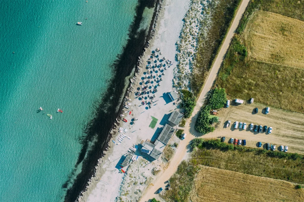 Vue aérienne verticale d'une plage de sable fin, d'un club de glisse et d'une eau turquoise transparente à Limnos en Grèce.