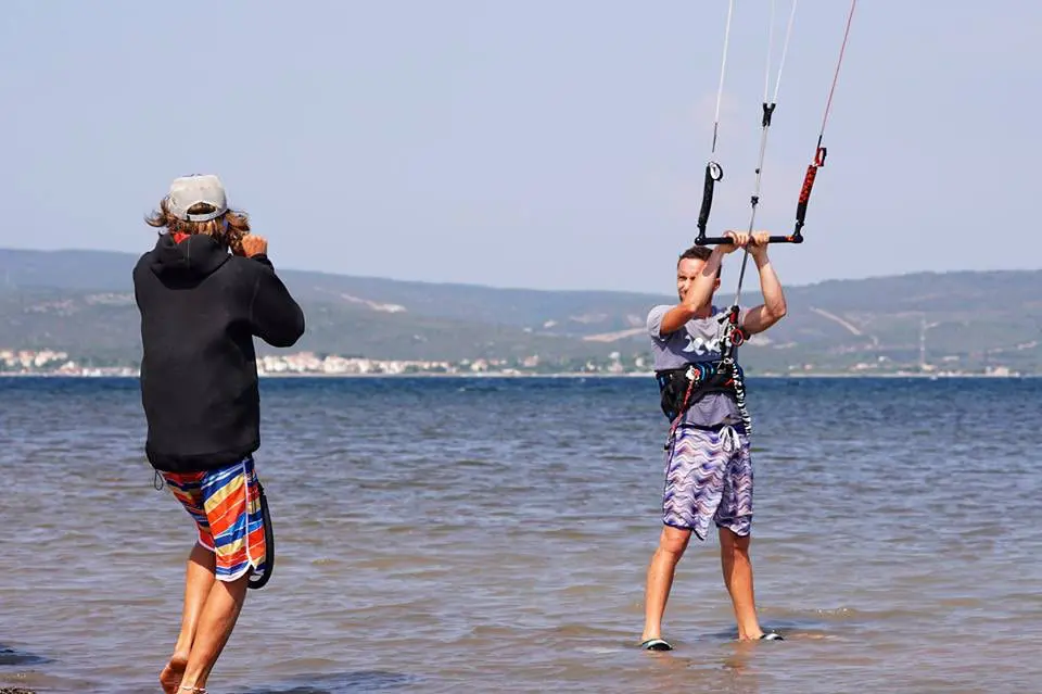 Un moniteur donne des instructions à un pratiquant debout dans l'eau peu profonde tenant sa barre de kitesurf à Urla en Turquie.