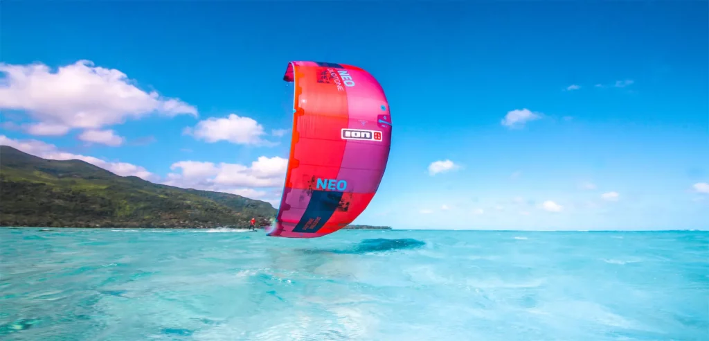 Une aile de kitesurf rose et rouge Duotone Neo survole un lagon d'eau transparente turquoise face aux montagnes de l'Île Maurice.