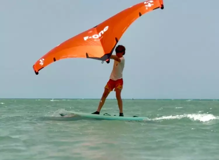 Un garçon navigue en wingfoil sur l'eau avec une aile orange de marque F-One.